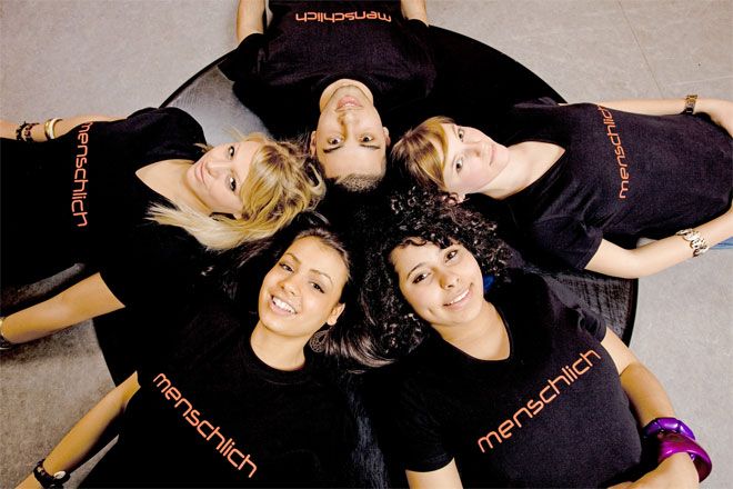 Bild: Fünf Jugendliche liegen Kopf an Kopf im Kreis. Sie lachen und wirken vergnügt und herzlich. Alle tragen ein schwarzes T-Shirt mit der Aufschrift 'menschlich'.